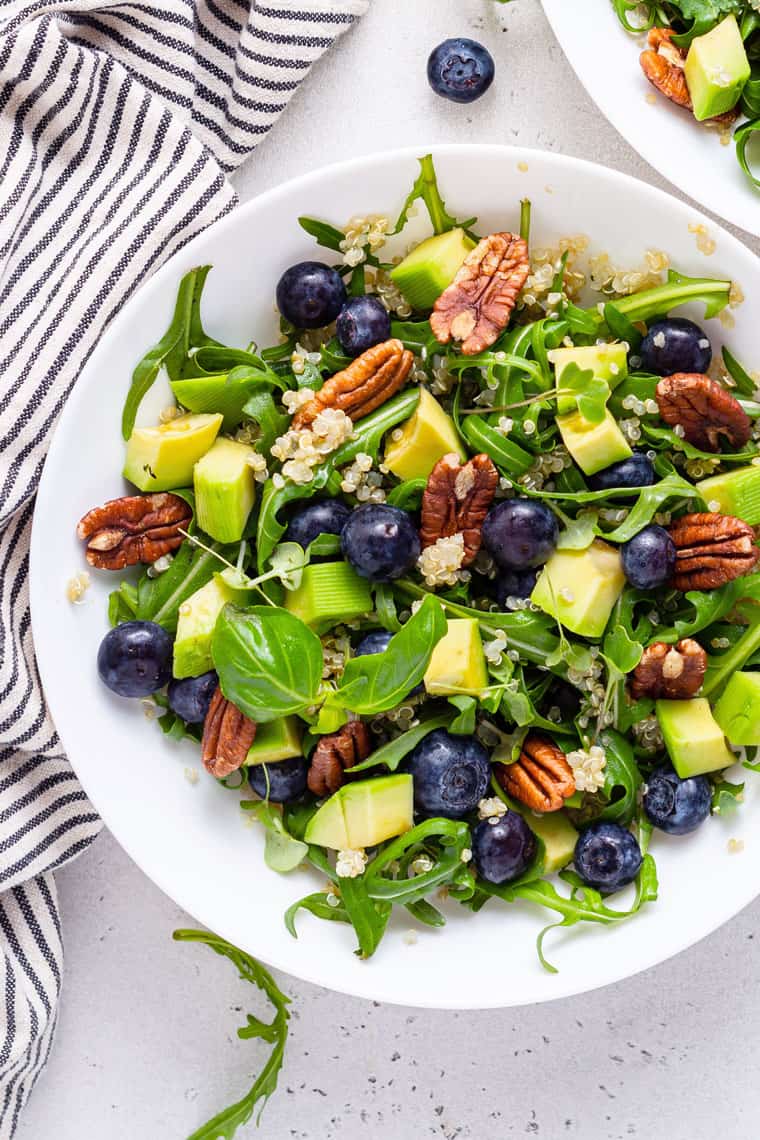 overhead of a white bowl with blueberry, arugula and quinoa salad