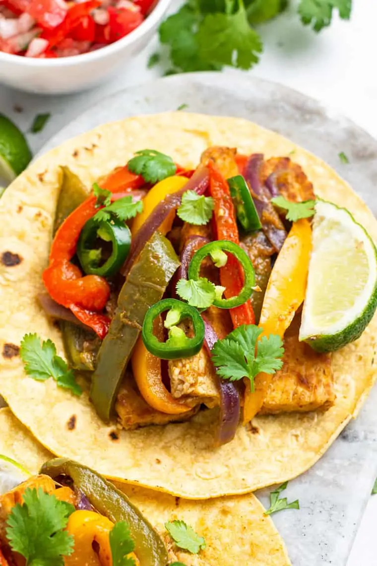 close up on a tempeh fajita with peppers, lime and jalapenos