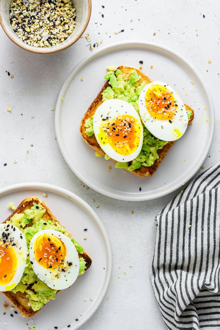 two plates of avocado toast with soft boiled eggs on top