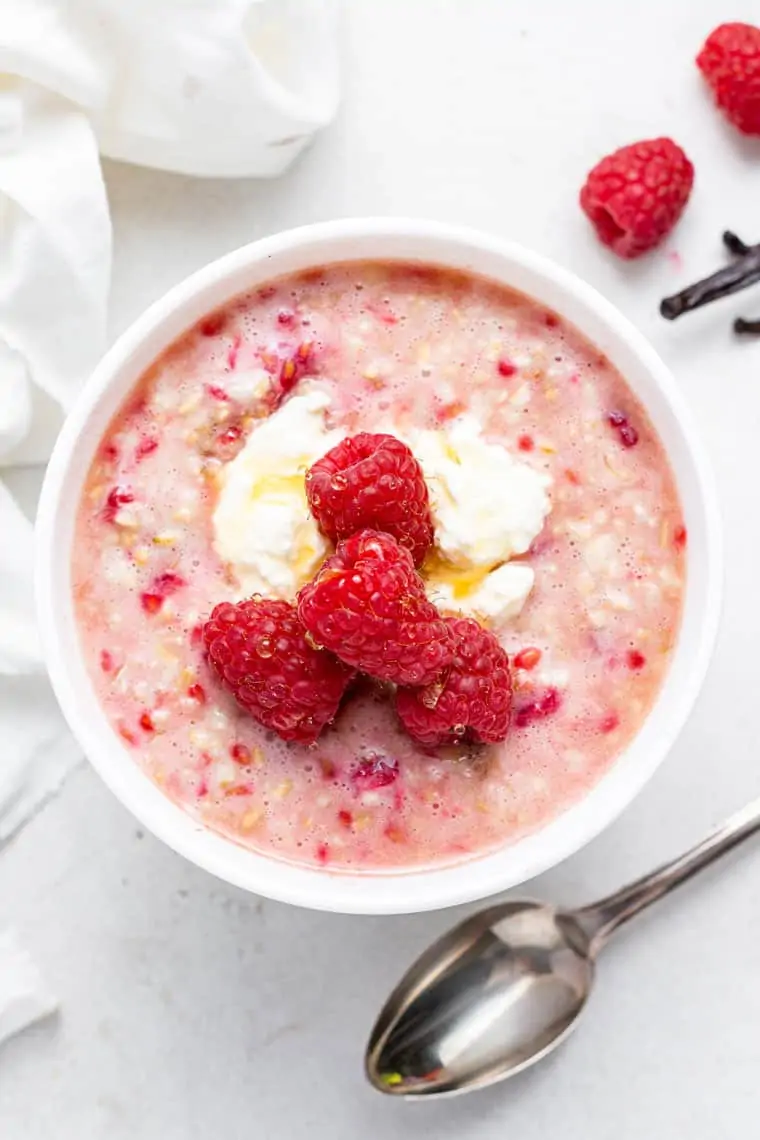 white bowl of pink overnight steel cut oats with raspberries and vanilla