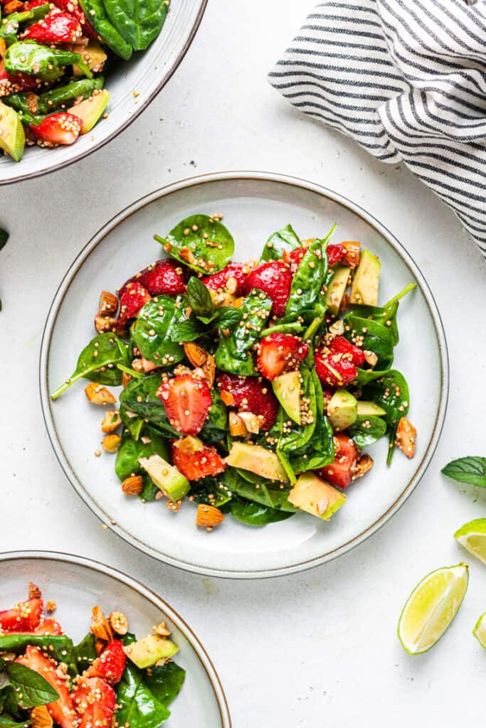 Overhead view of a serving of strawberry spinach salad with avocado, almonds, and toasted quinoa with honey lime dressing on a plate.