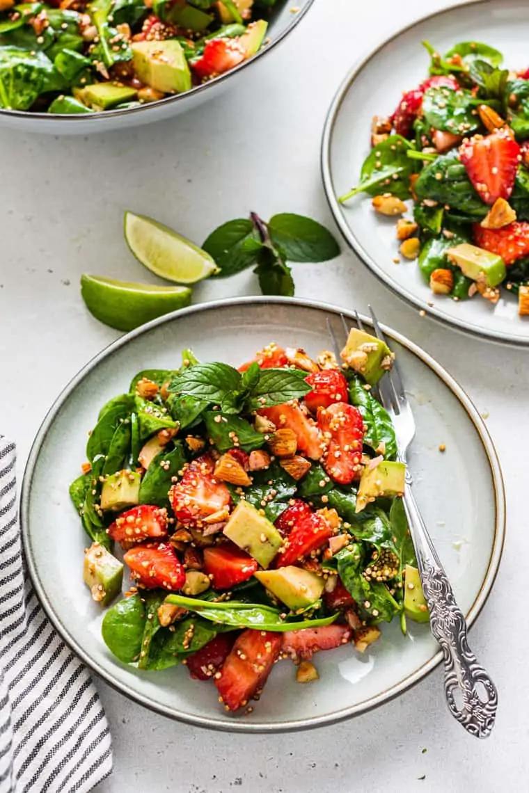 two plates of strawberry avocado and spinach salad with a fork