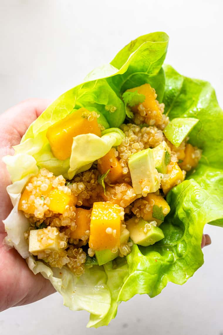 hand holding a lettuce leaf filled with mango and quinoa salad