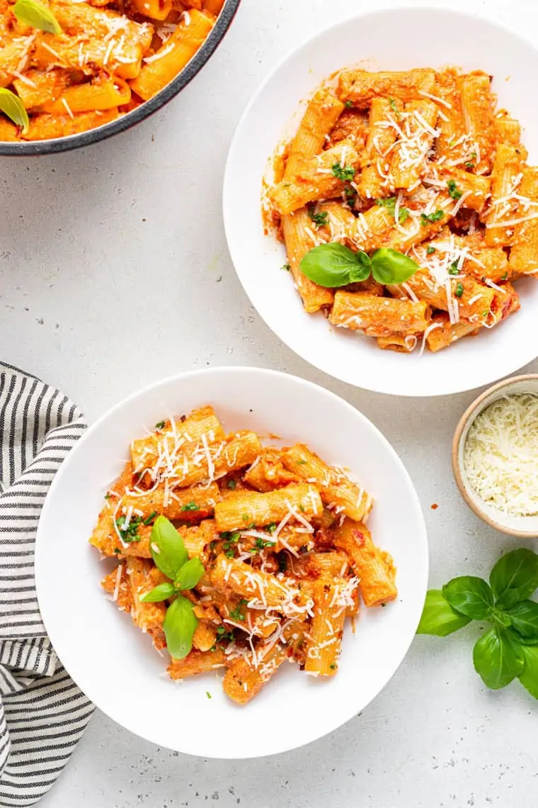 two plates of vegan vodka sauce pasta with fresh basil and grated cheese on top