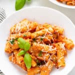 white plate with vegan vodka pasta sauce served over rigatoni noodles with basil and grated cheese