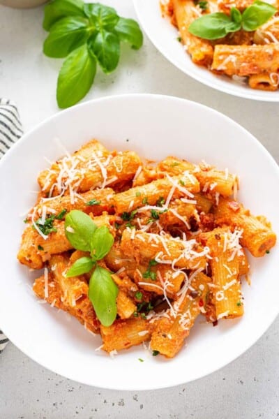 white plate with vegan vodka pasta sauce served over rigatoni noodles with basil and grated cheese
