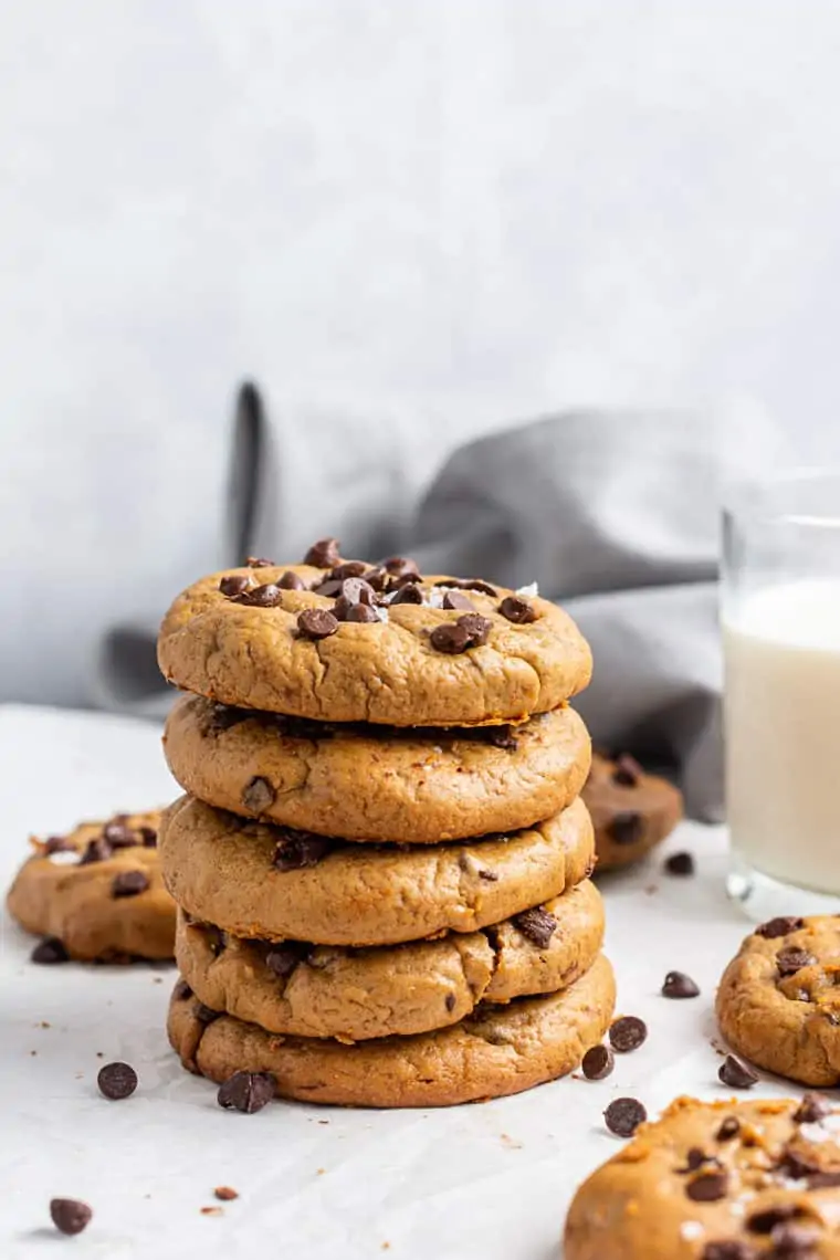 stack of several almond butter chocoalte chip cookies with a glass of milk