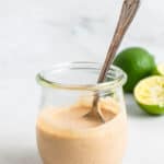 glass jar of tahini lime dressing with a silver spoon