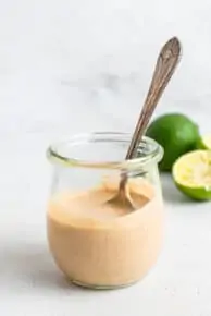 glass jar of tahini lime dressing with a silver spoon