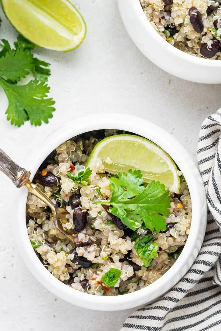 overhead of a white bowl with quinoa and bean salad and fresh limes