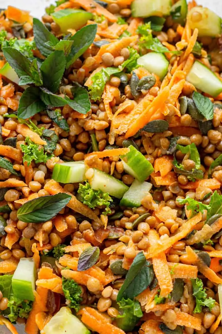 close up on lentil salad in clear bowl with cucumbers and carrots