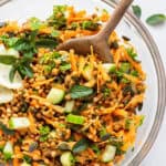 overhead of lentil salad with carrots served in a clear glass bowl with wooden spoon