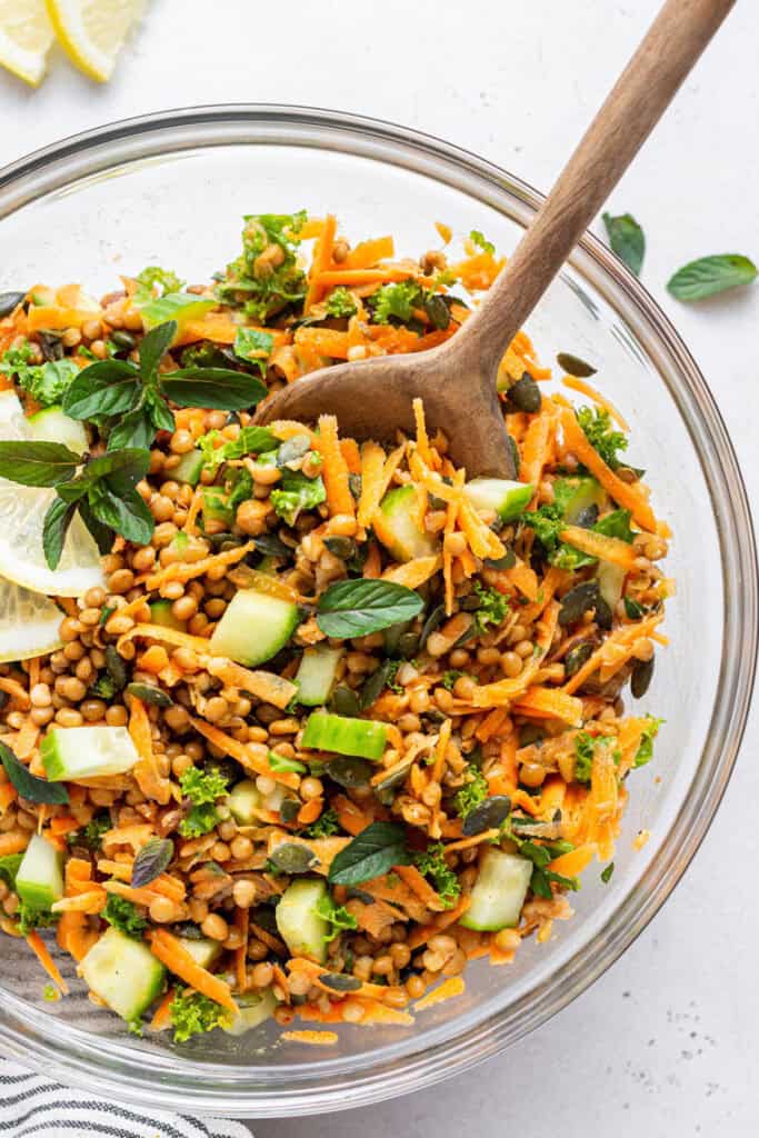 overhead of lentil salad with carrots served in a clear glass bowl with wooden spoon