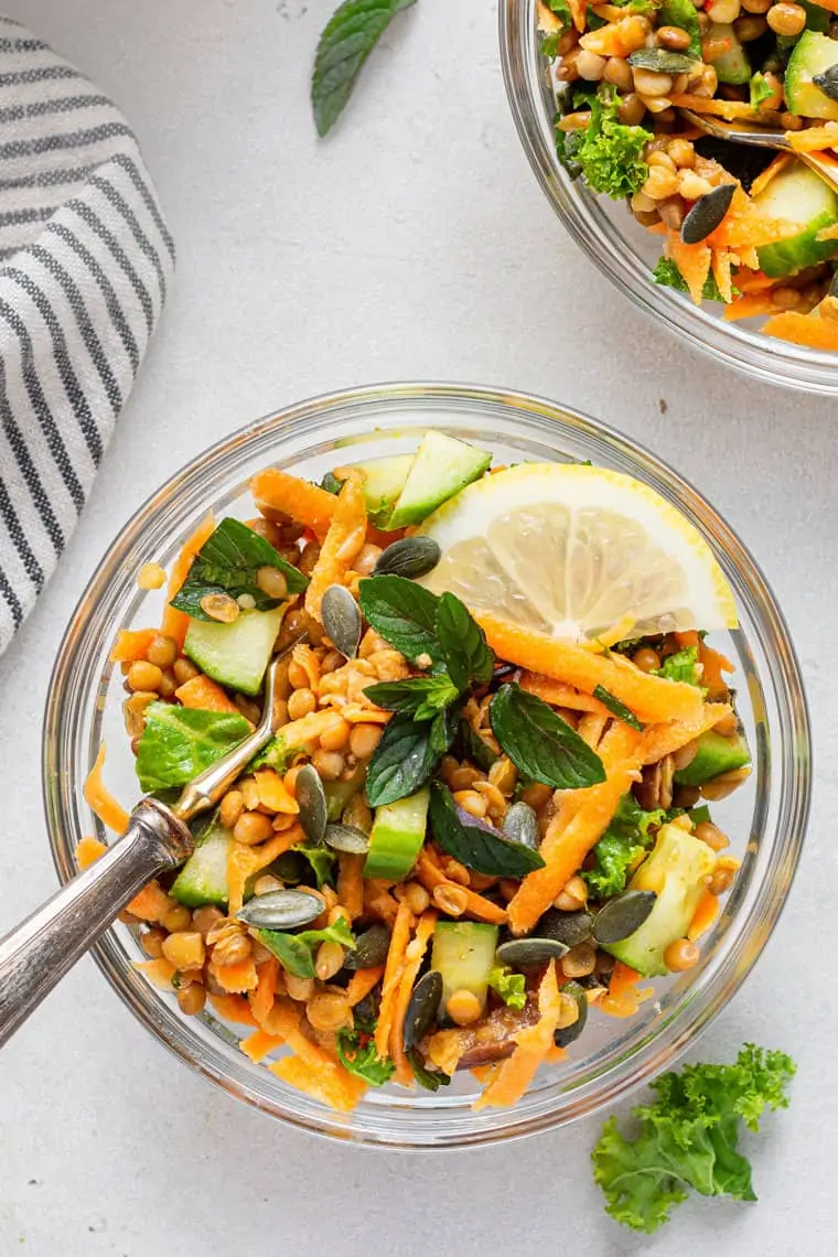 Overhead view of lentil salad in two glass bowls, garnished with mint and lemon slice