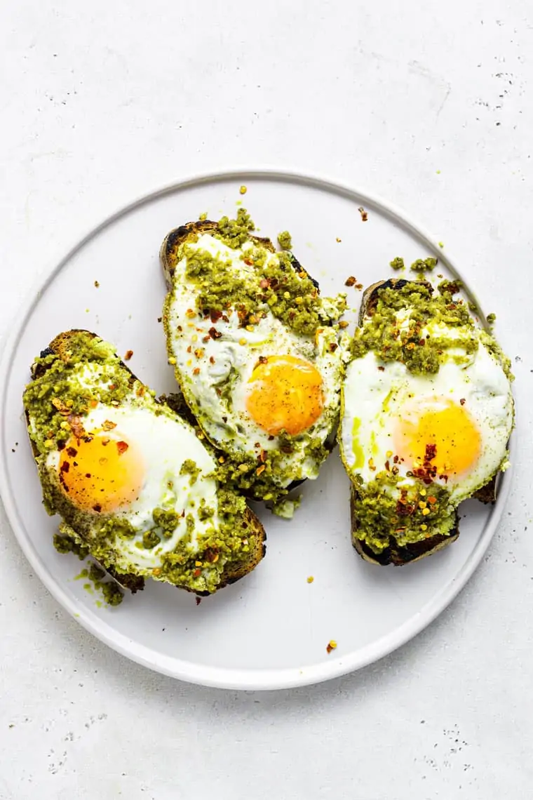 plate with three slices of toast with pesto eggs on top