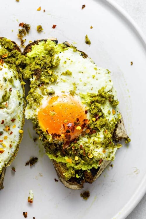 close up on a slice of toast with pesto and a fried egg with red pepper flakes