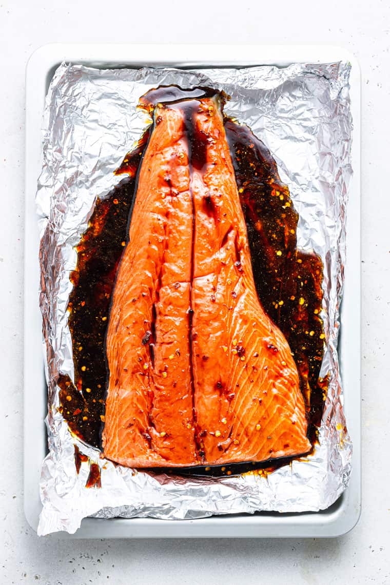 Large piece of salmon on a pice of foil covered in brown and red sauce
