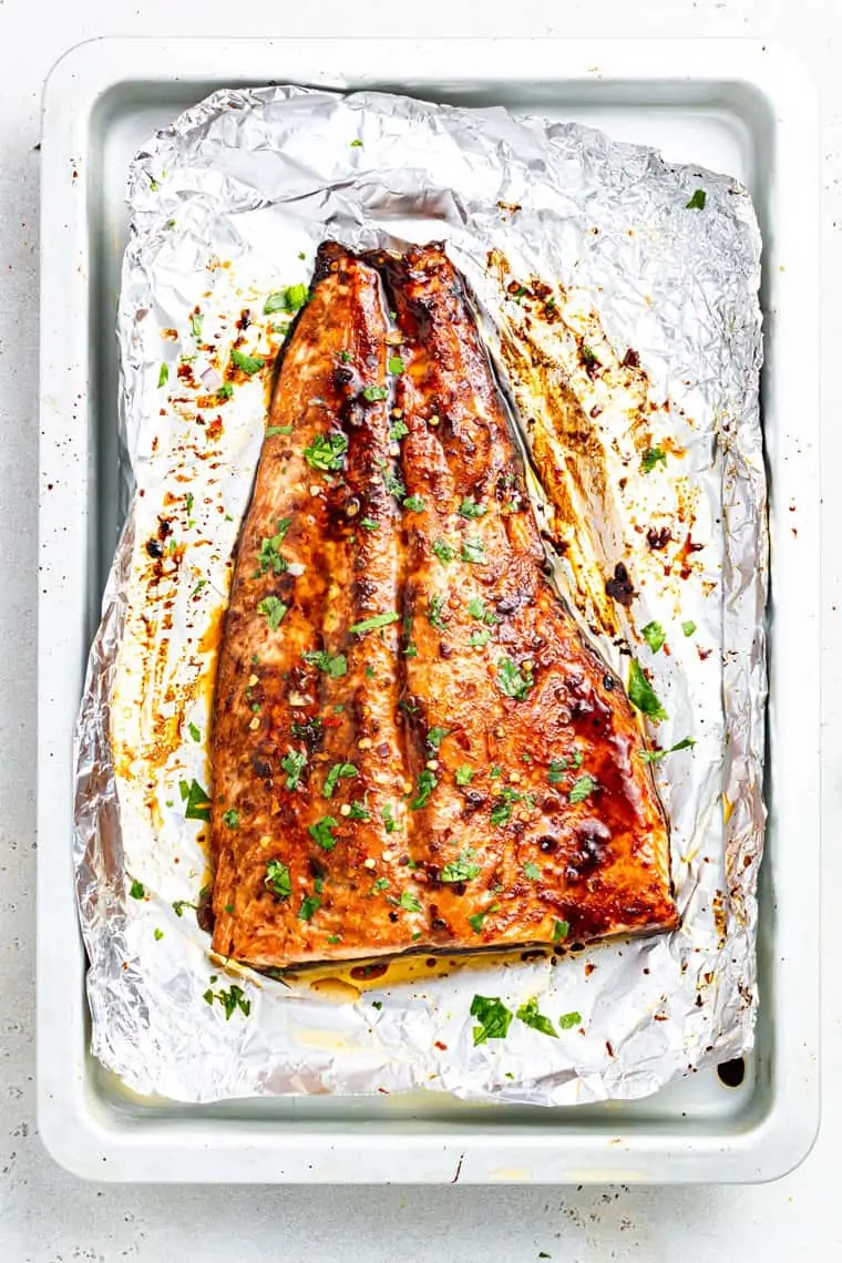 cooked side of salmon on a piece of foil with green herbs on top