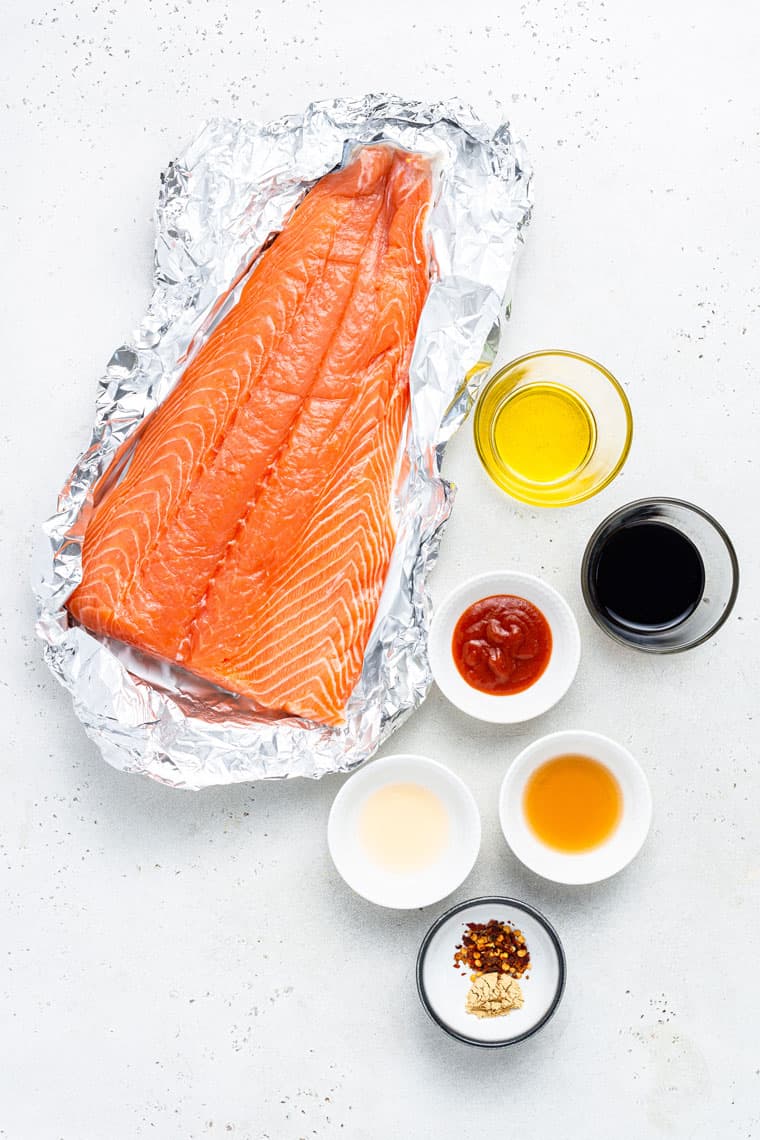 large piece of salmon in a foil wrapper with ingredients for sauce in small bowls on the side