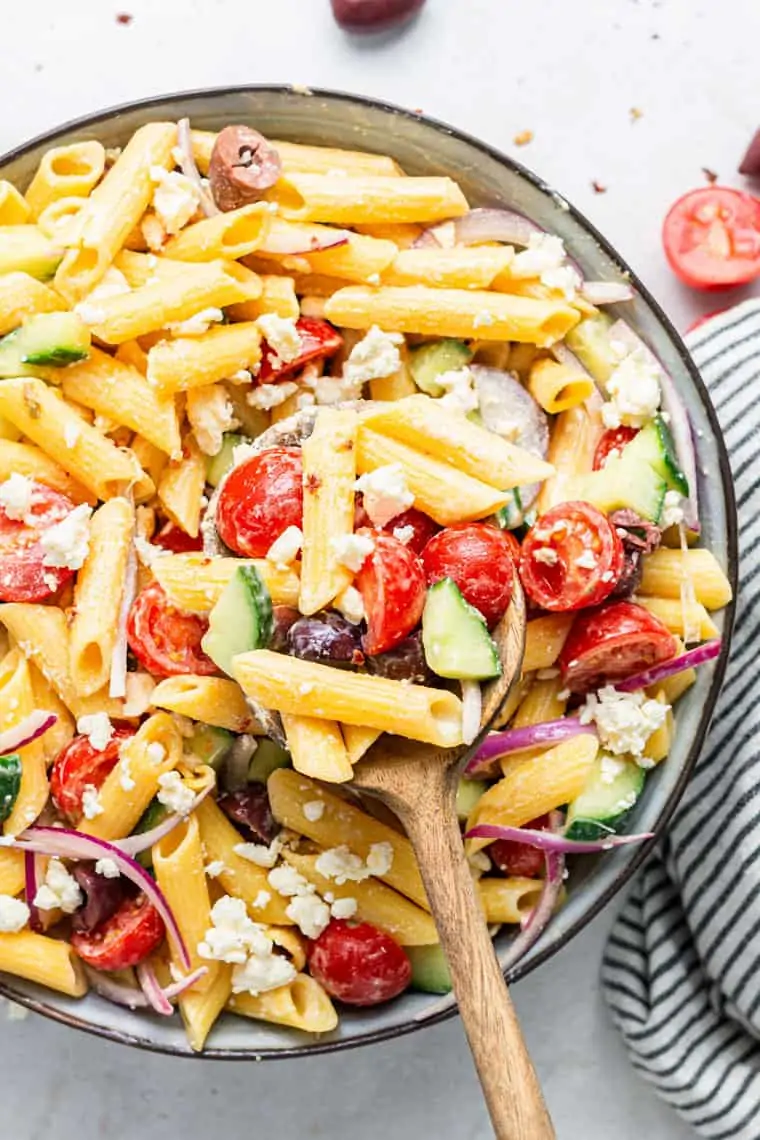 stirring pasta salad with raw vegetables and olives