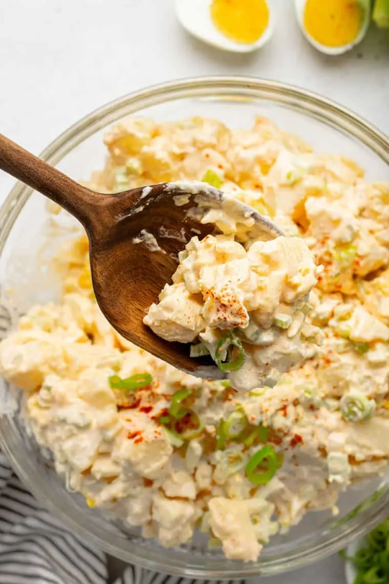 A wooden spoon pulling a spoonful of potato salad out of a mixing bowl