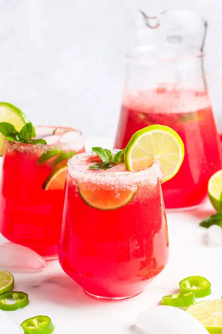 two glasses and a pitcher of watermelon margarita with lime juice and a salt rim