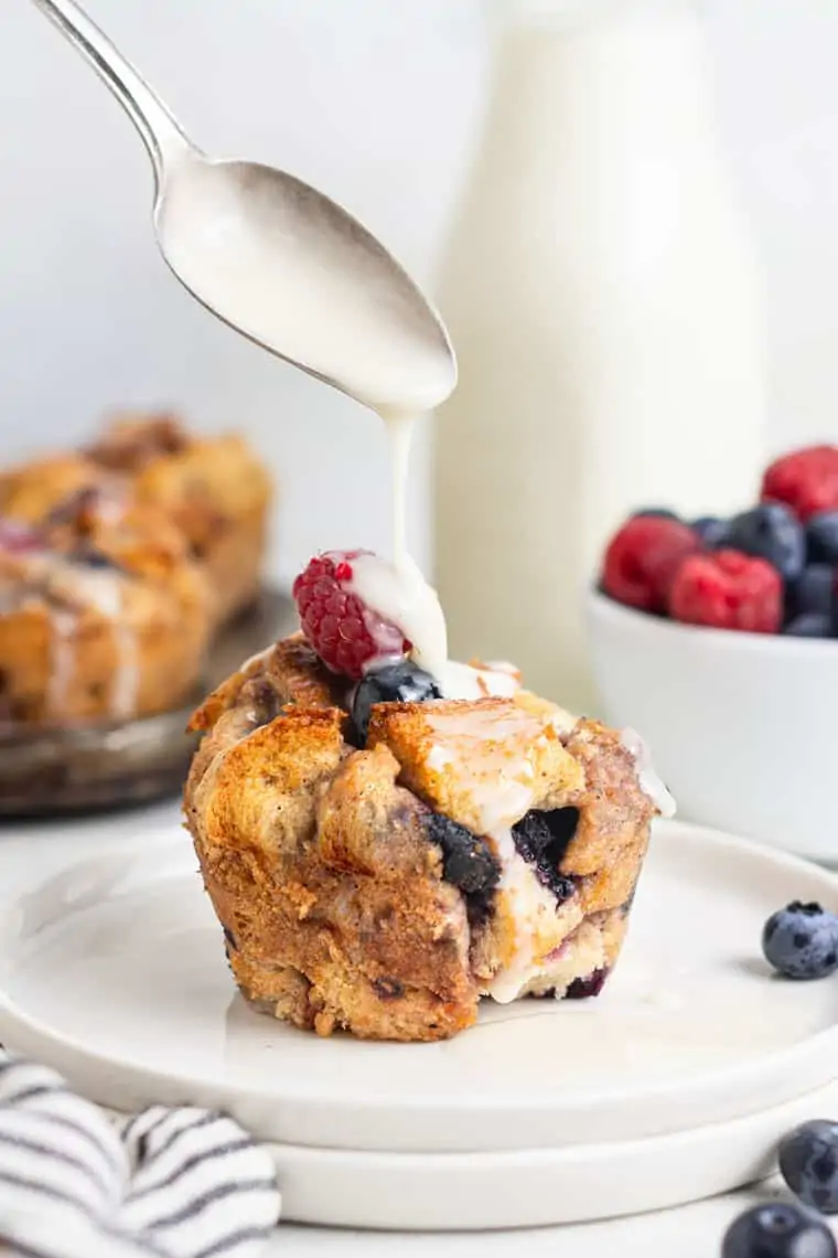 pouring glaze over a berry french toast cup on a plate