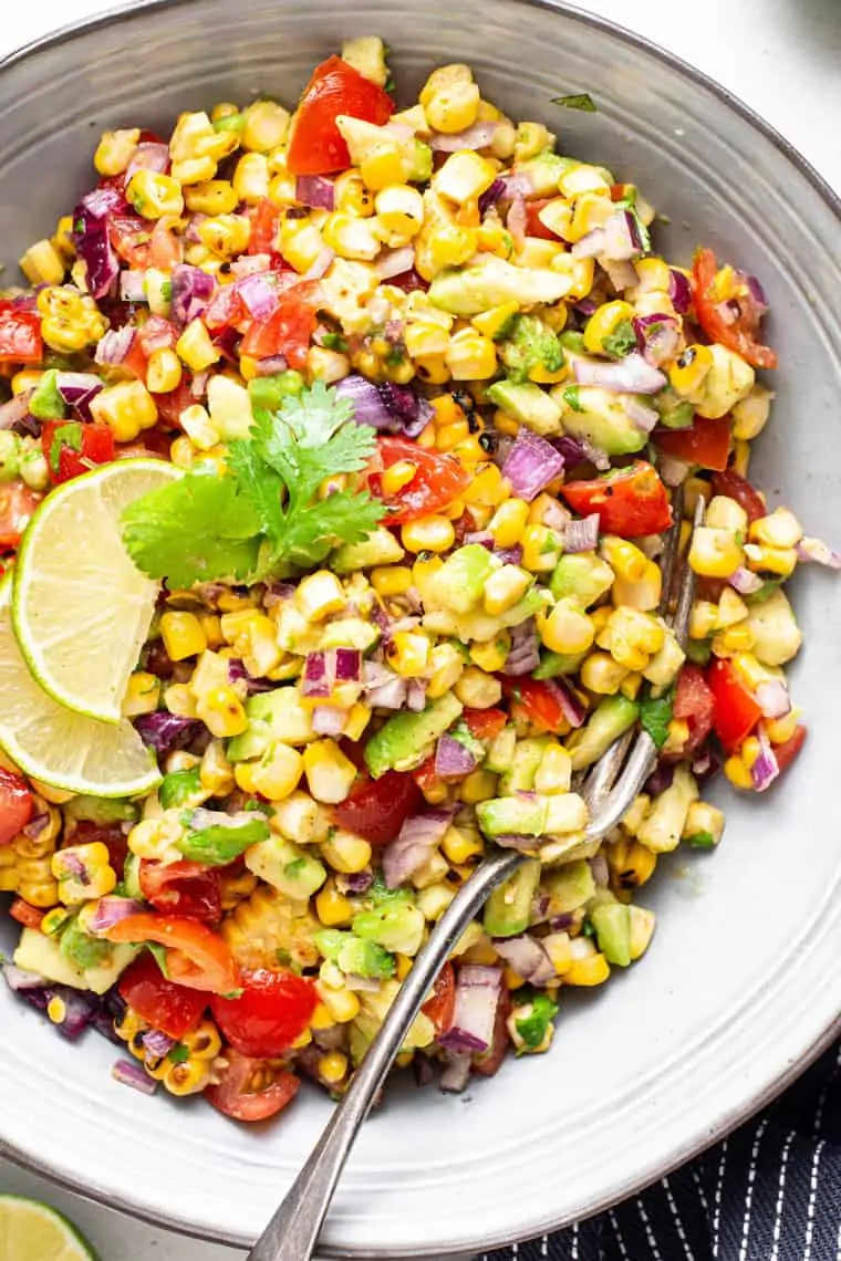 bowl of corn and avocado salsa with tomatoes and lime