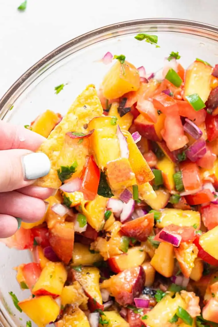 hand scooping peach salsa on a chip