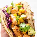 close up on a salmon and mango taco with cilantro, cabbage and lime