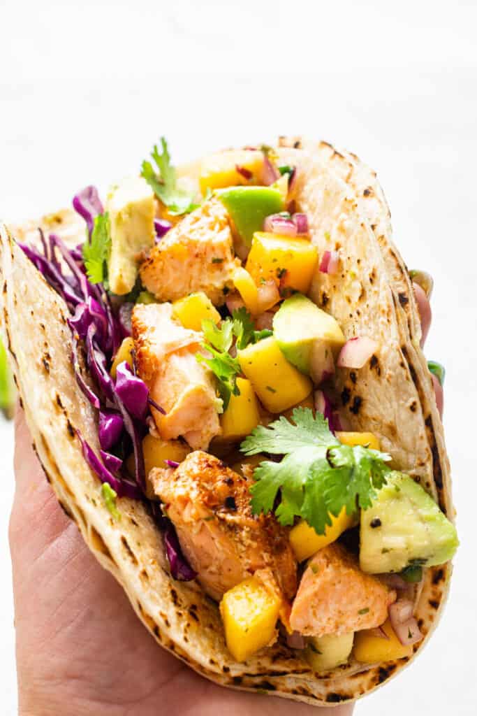 close up on a salmon and mango taco with cilantro, cabbage and lime