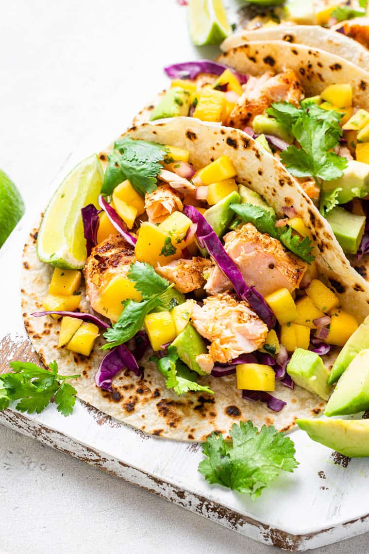 salmon tacos on a plate with fresh mango, lime, cilantro and purple cabbage