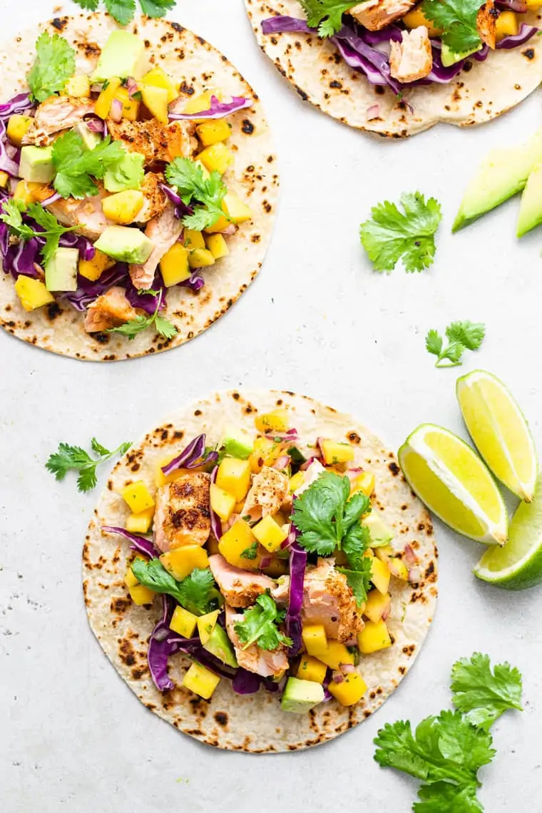 overhead of three tortillas with salmon, mango, lime and cilantro