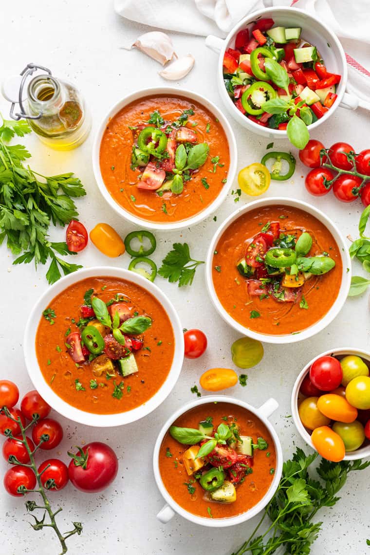 four bowls of tomato gazpacho with fresh tomatoes and herbs