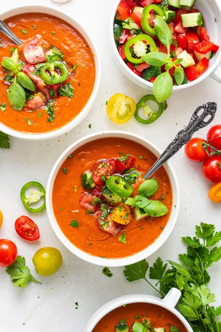 three bowls of tomato gazpacho with sliced vegetables and herbs
