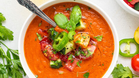 bowl of spicy gazpacho with a jar of olive oil and fresh herbs