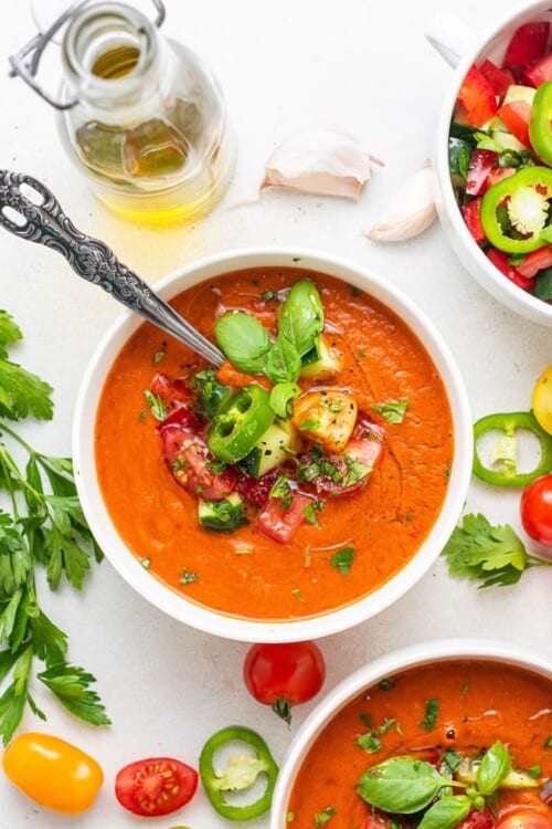 bowl of spicy gazpacho with a jar of olive oil and fresh herbs