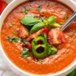 close up on tomato gazpacho ina white bowl with fresh herbs
