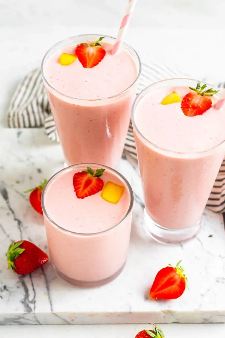 three glasses of pink smoothies with strawberries
