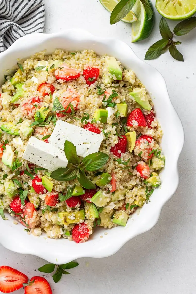 white bowl of strawberry quinoa salad with cheese, avocado and lime juice