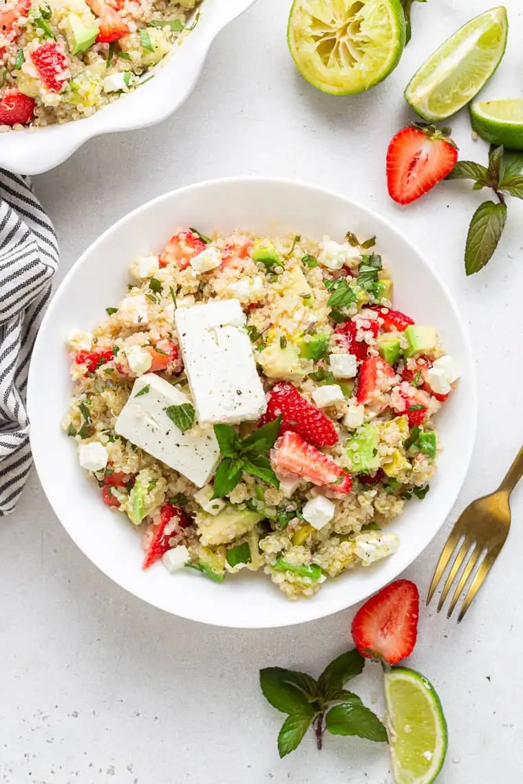 overhead of a white bowl with quinoa, strawberry, avocado, mint and lime salad