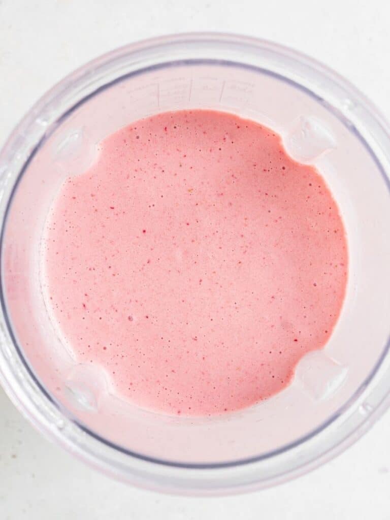 Make this strawberry mango smoothie with dairy-free yogurt, nut butter, chia seeds, and frozen fruit for a filling, high-protein breakfast. Overhead view of a blended strawberry mango smoothie in the blender.