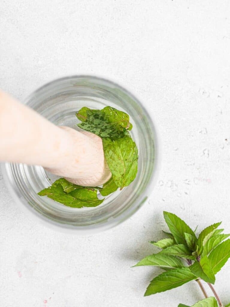 This peach mojito recipe is made with peach purée, white rum, lime, and fresh mint, sweetened with honey for a light, fizzy summer cocktail. Using a muddler to muddle mint leaves in the bottom of a glass.