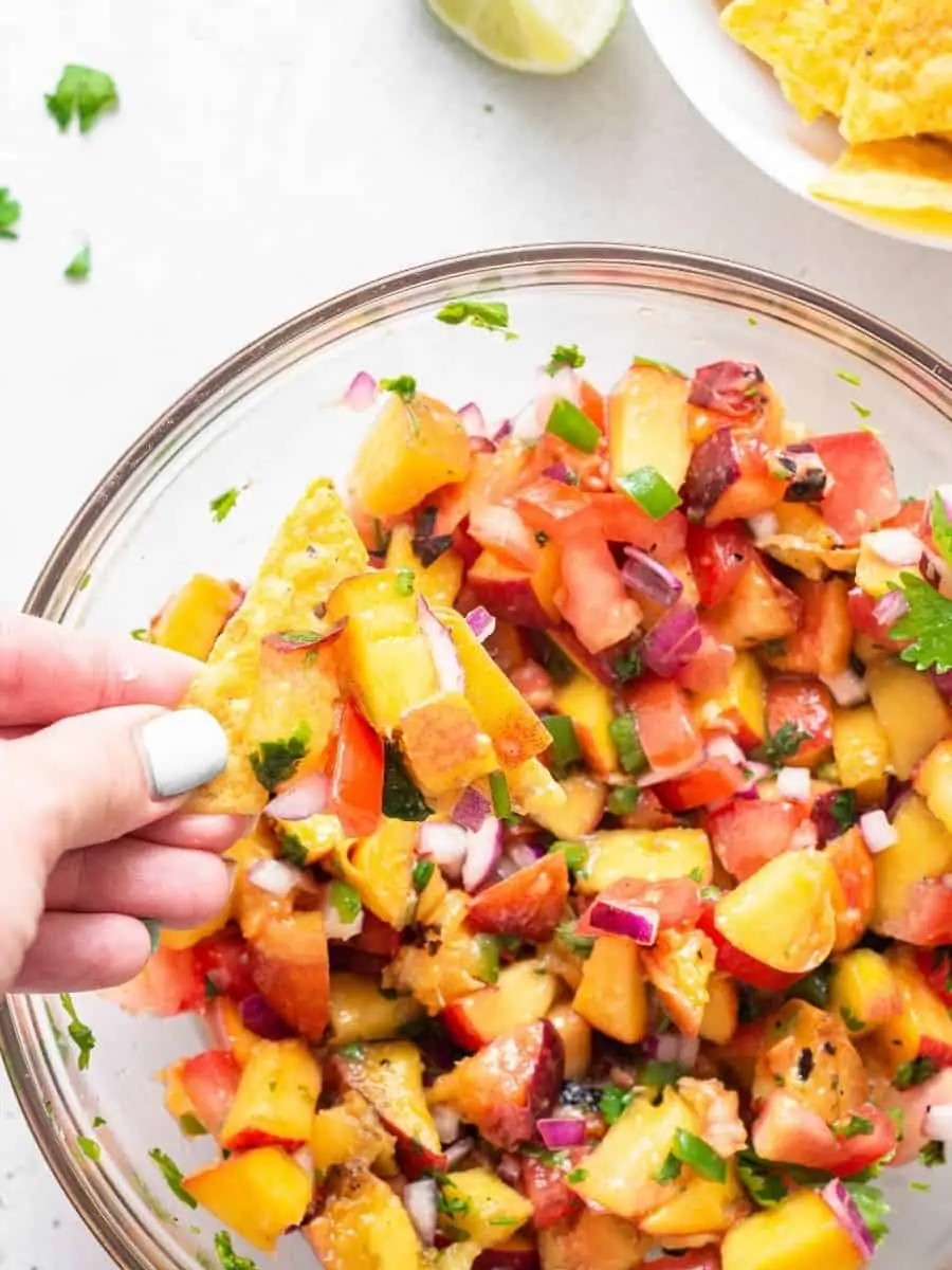 This refreshing Peach Salsa recipe is a sweet, savory and spicy homemade condiment you’ll love with fish, chips and more. Easy and delicious! Hand holding chip with peach salsa