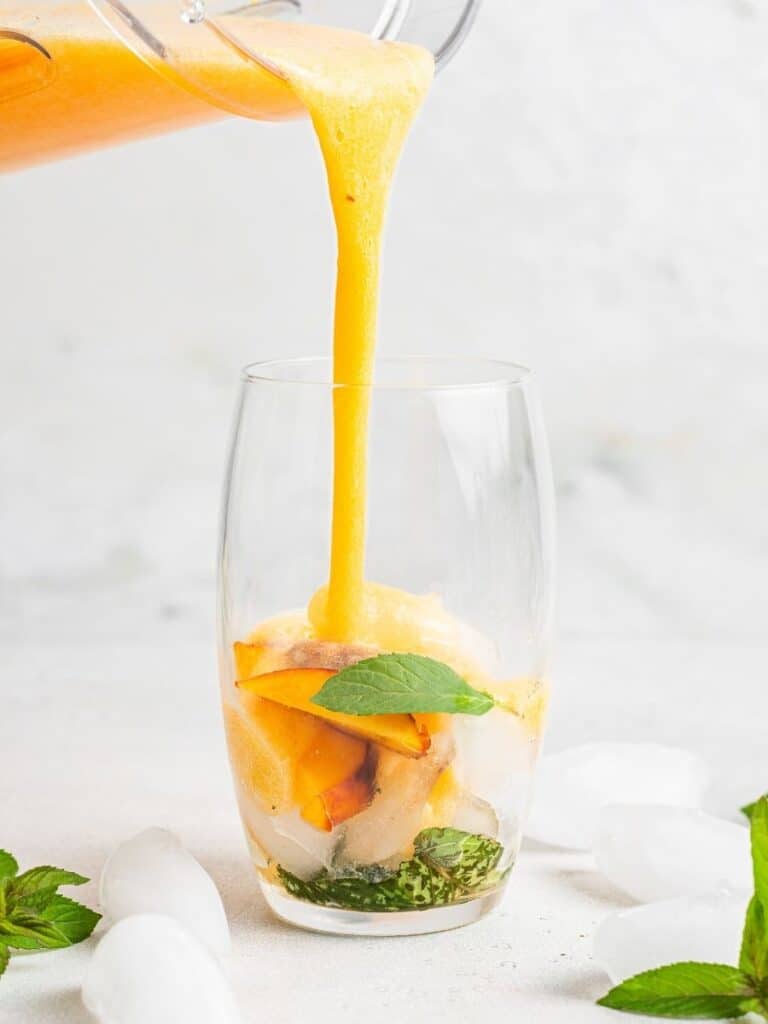 This peach mojito recipe is made with peach purée, white rum, lime, and fresh mint, sweetened with honey for a light, fizzy summer cocktail. Pouring peach mojito mixture into a glass of ice.
