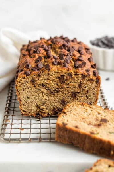 whole loaf of chocolate chip zucchini bread with a slice removed on a wire rack