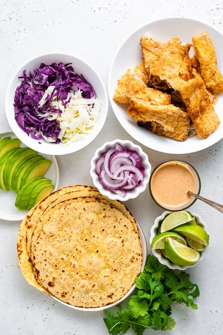 bowls with crispy breaded fish, cabbage, avocado, and tortillas