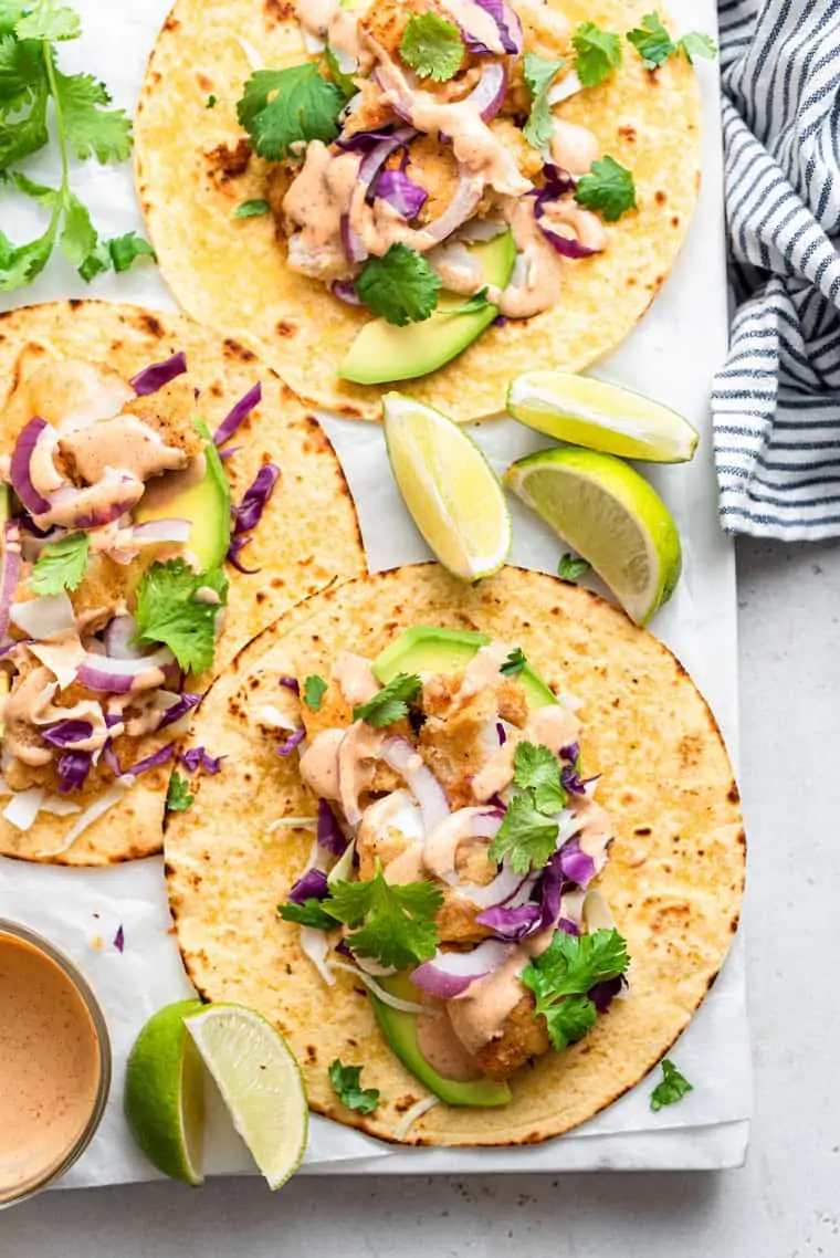 white board with three crispy fish tacos on tortillas