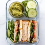 overhead of a glass bento box with cucumber and guacamole sandwiches