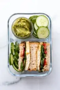 overhead of a glass bento box with cucumber and guacamole sandwiches